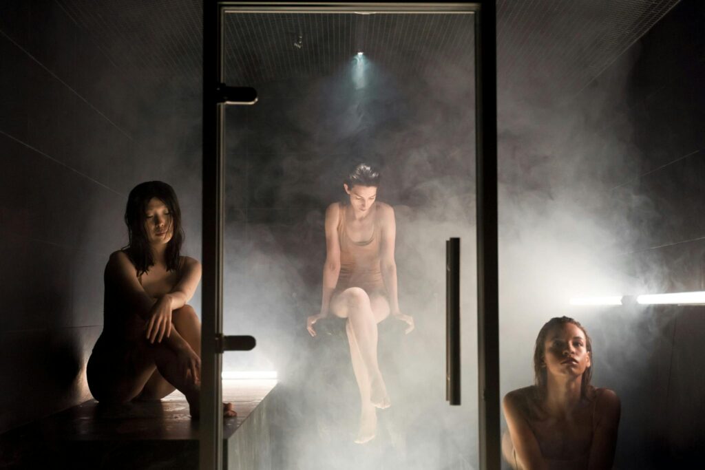 Three women enjoying the calming atmosphere of a steam-filled sauna for relaxation and wellness.